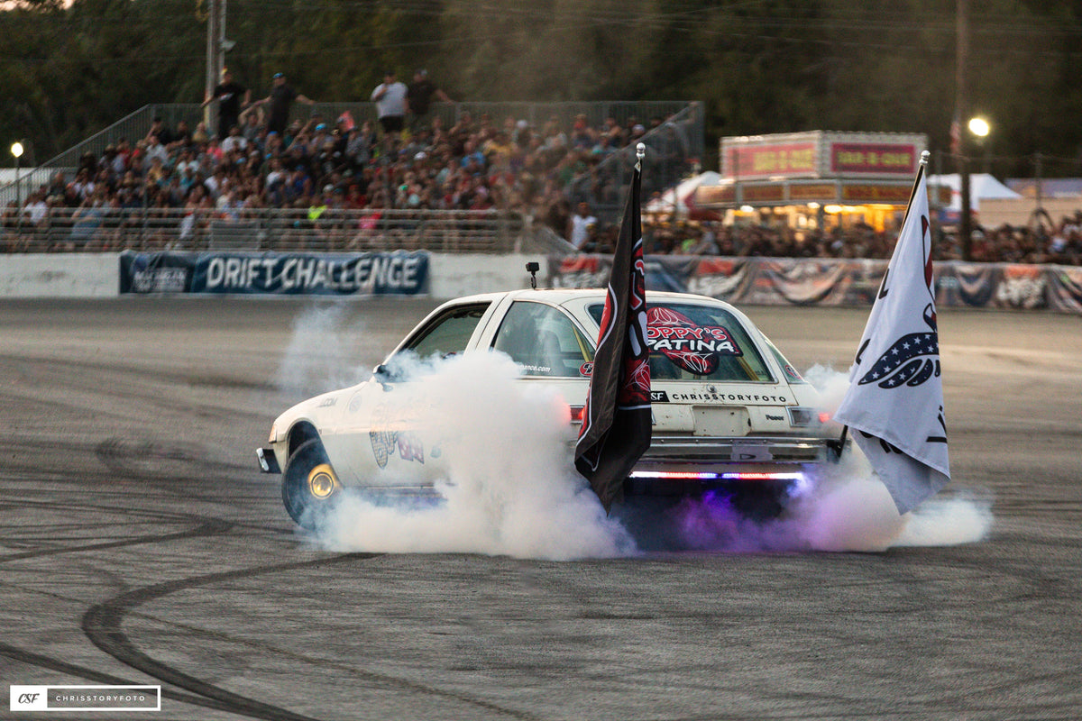 Pit Boss AMC Pacer spinning a burnout with purple underglow and flags flying