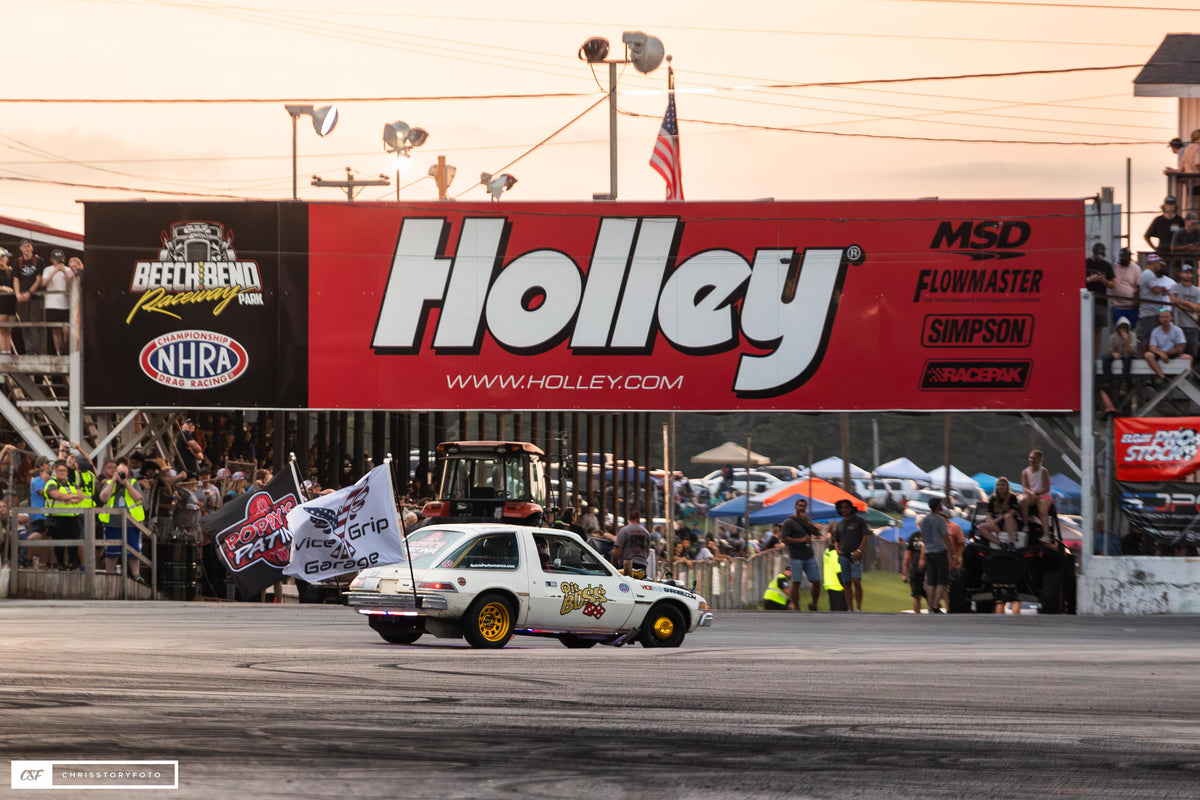 Pit Boss AMC Pacer with team flags in front of a Holley banner and grandstand