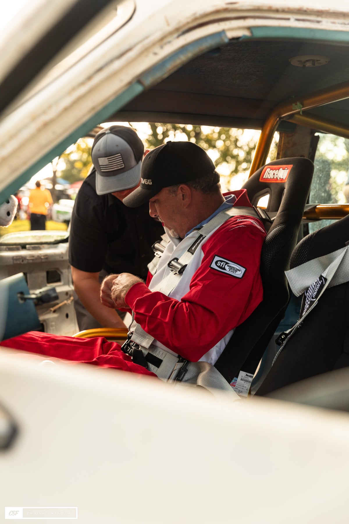 Crew member helping the driver into the harness in the Pit Boss cockpit
