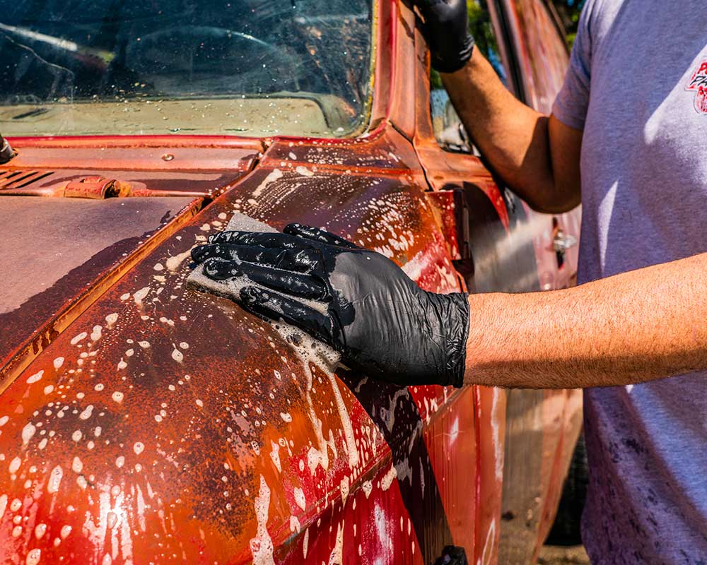 Gloved hand prepping a red patina van with a soapy scuff pad